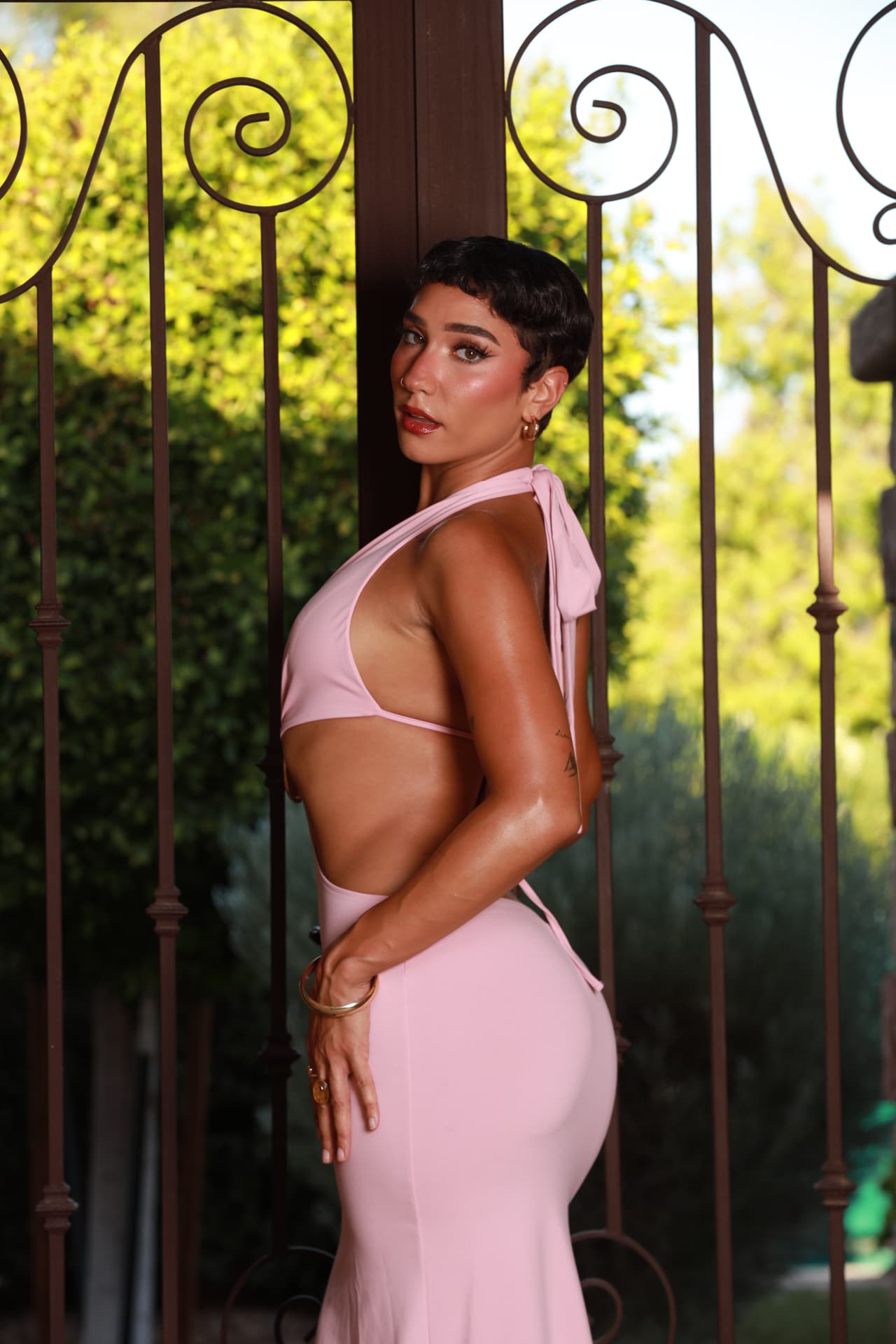 Aryanna, founder of Arys Grrls, in a pink halter gown beside an iron gate